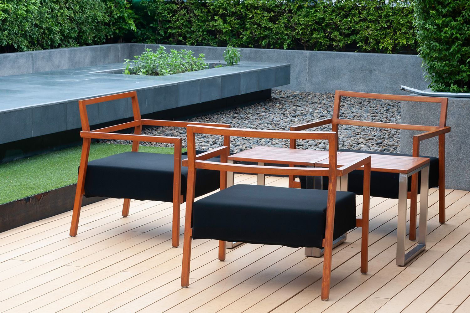 Three modern wooden chairs with black seats and two small tables on a wooden deck. Three modern wooden chairs with black seats and two small tables on a wooden deck.