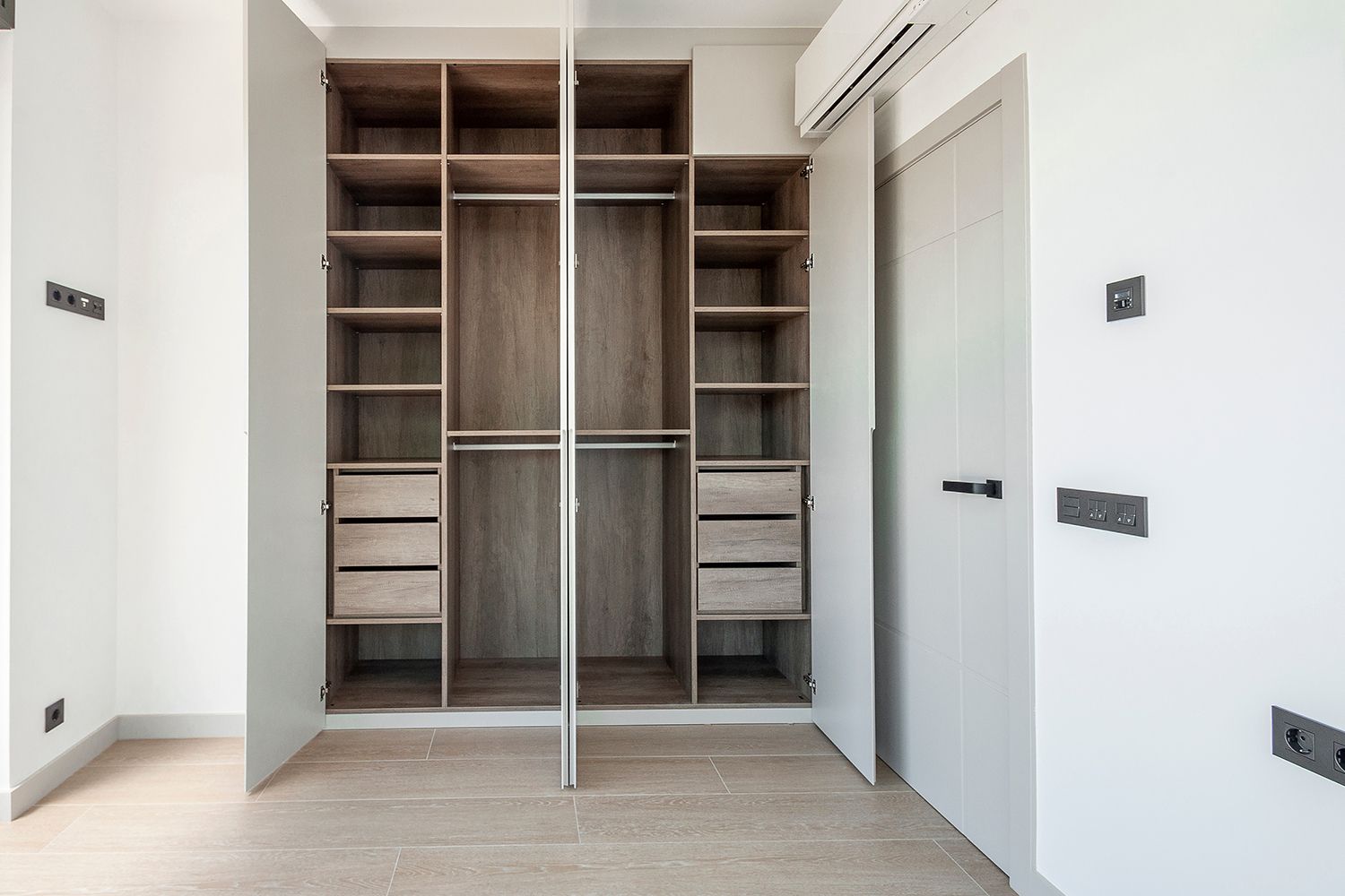 Open, built-in closet with shelves and drawers. Light wood interior, white doors, and a door on the right.