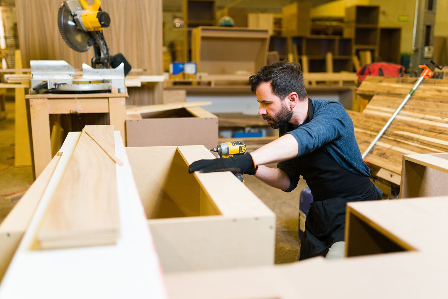 Man in workshop assembling wooden furniture with a power drill. Man in workshop assembling wooden furniture with a power drill.