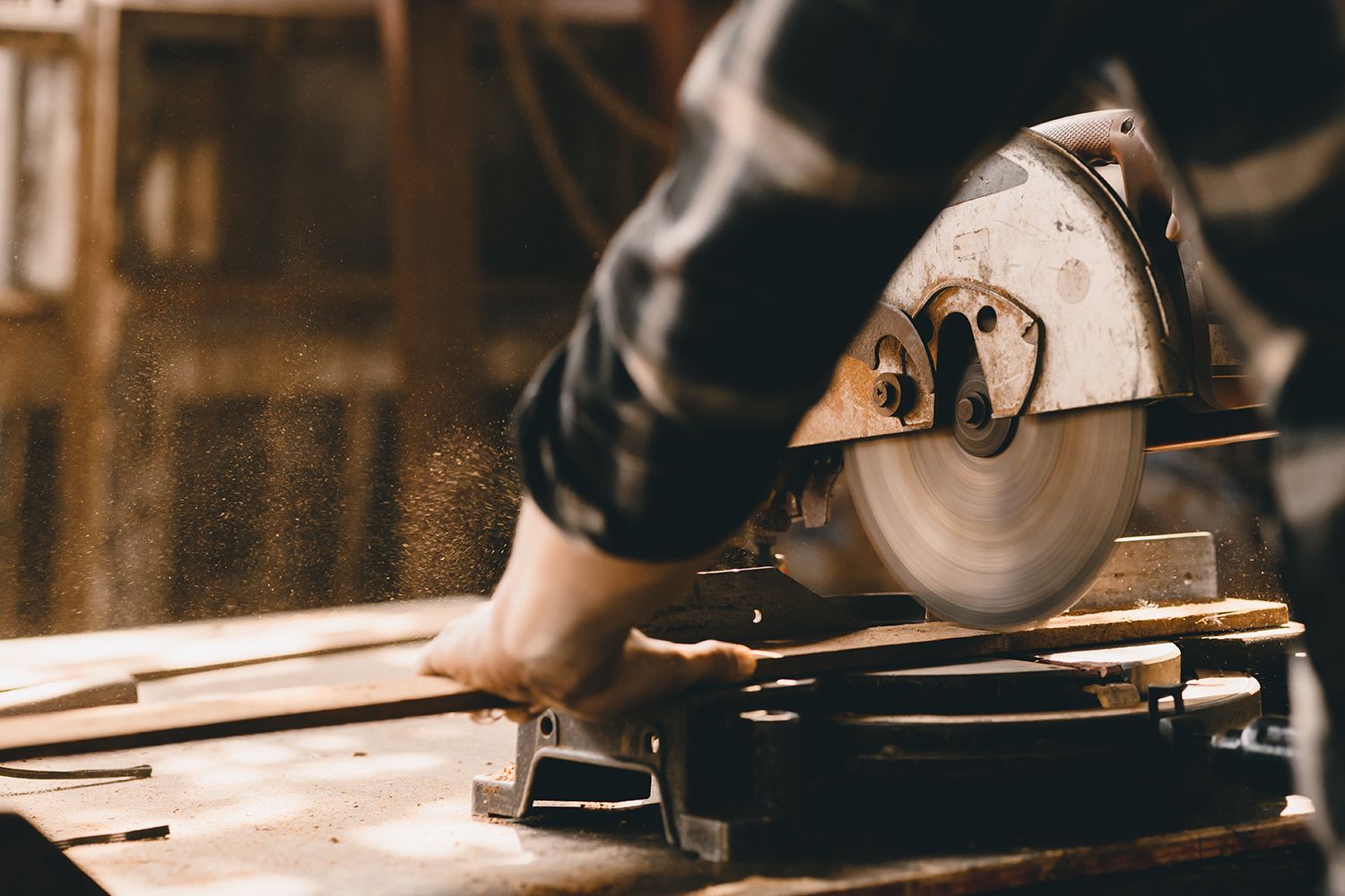 A person using a circular saw to cut wood in a workshop, sawdust in the air. A person using a circular saw to cut wood in a workshop, sawdust in the air.
