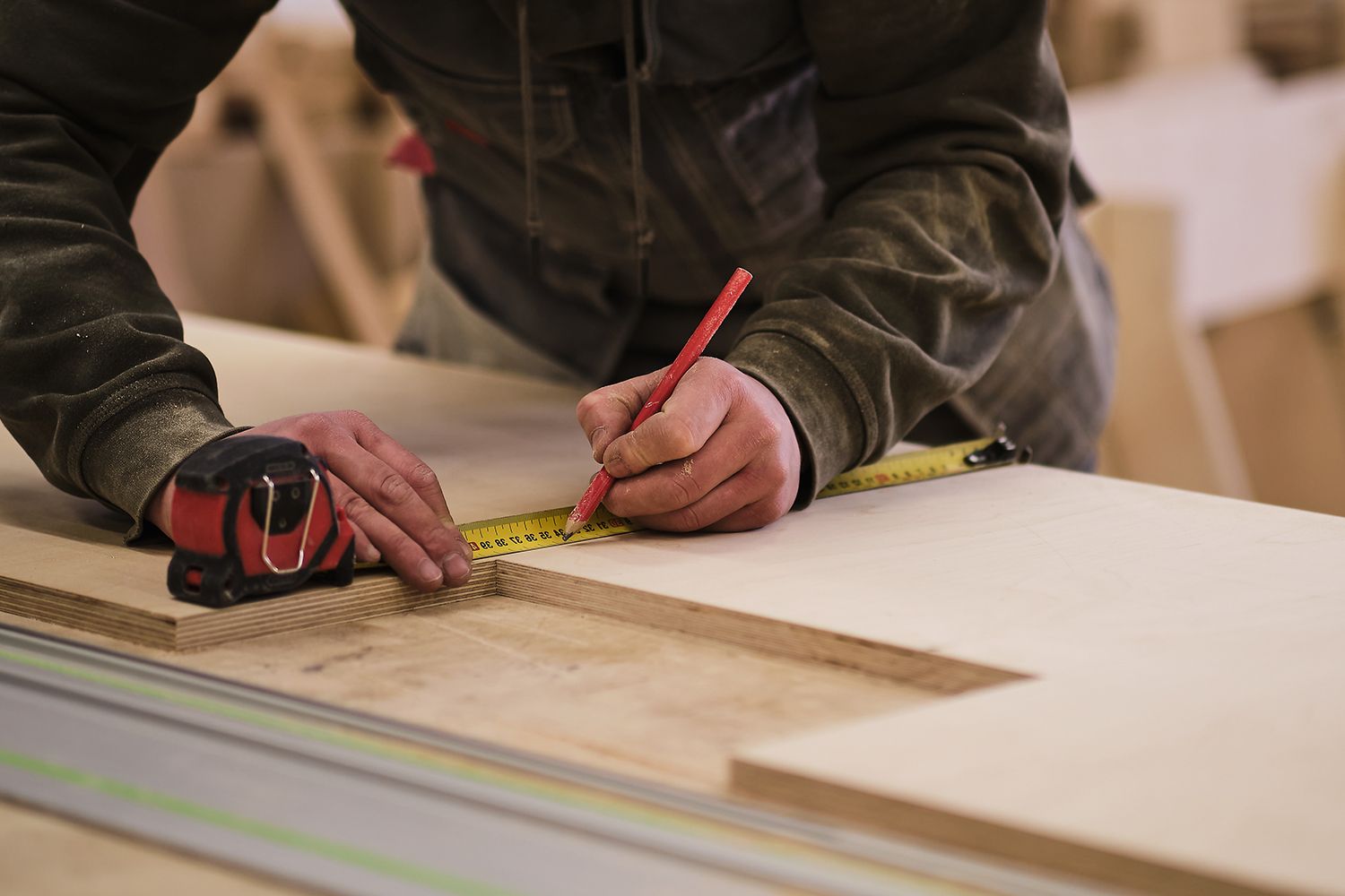 Carpenter using a pencil and tape measure to mark wood on a workbench. Carpenter using a pencil and tape measure to mark wood on a workbench.