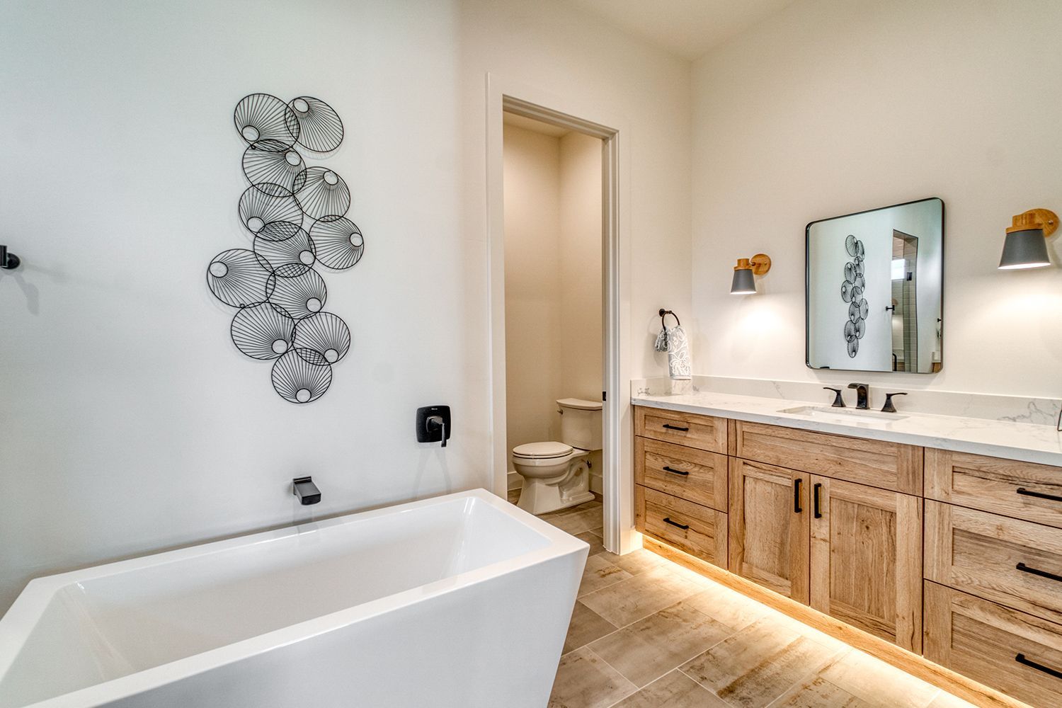 Modern bathroom with white tub, light wood vanity, and decorative wall art. Modern bathroom with white tub, light wood vanity, and decorative wall art.