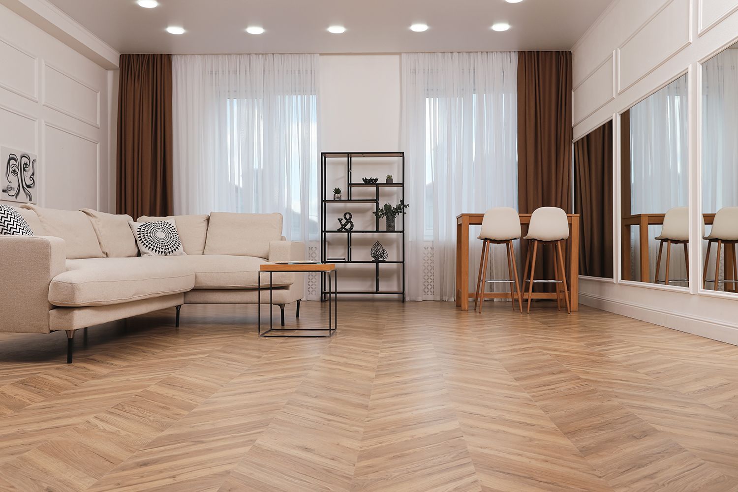 Living room with light-colored couch, wooden floor, large mirrors, and brown curtains. Living room with light-colored couch, wooden floor, large mirrors, and brown curtains.