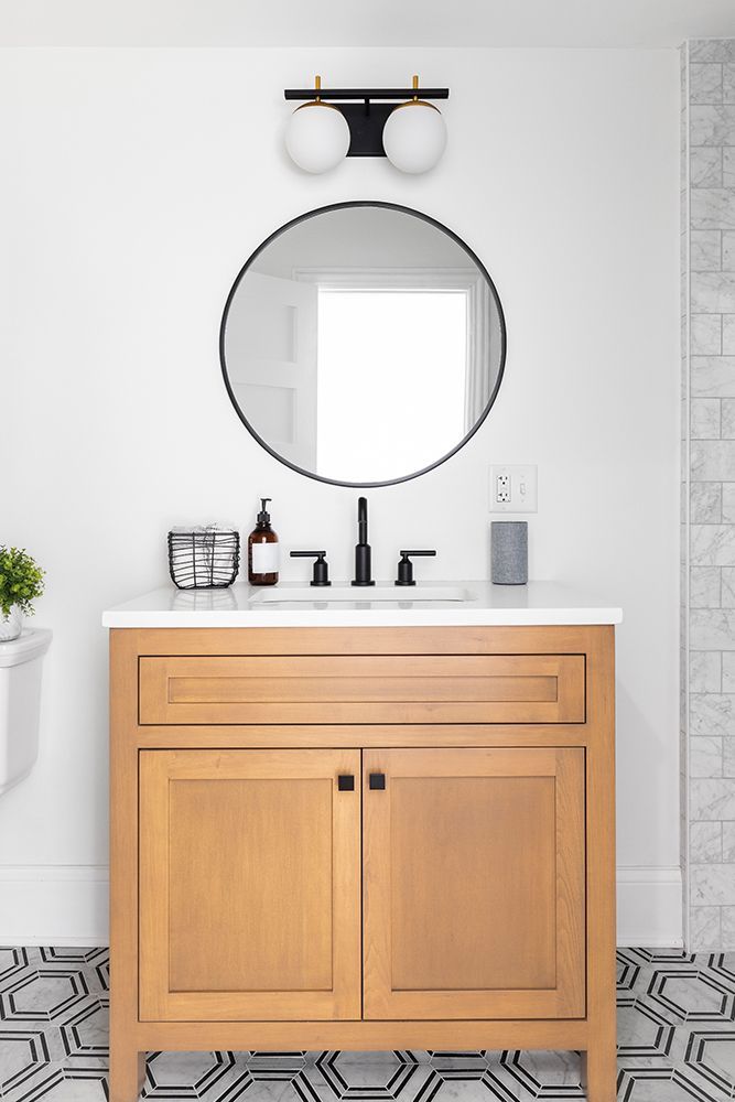 Bathroom vanity with round mirror, globe lights, and wood cabinet. Black and white patterned floor. Bathroom vanity with round mirror, globe lights, and wood cabinet. Black and white patterned floor.