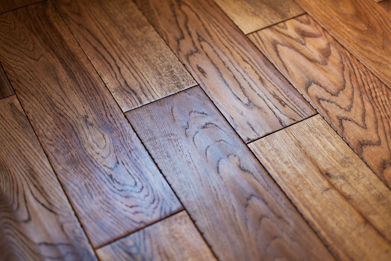 Close-up view of a hardwood floor with varying shades of brown and visible wood grain. Close-up view of a hardwood floor with varying shades of brown and visible wood grain.