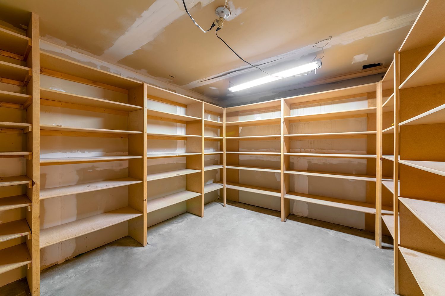 Empty pantry with light-colored wooden shelves on three walls; gray concrete floor.