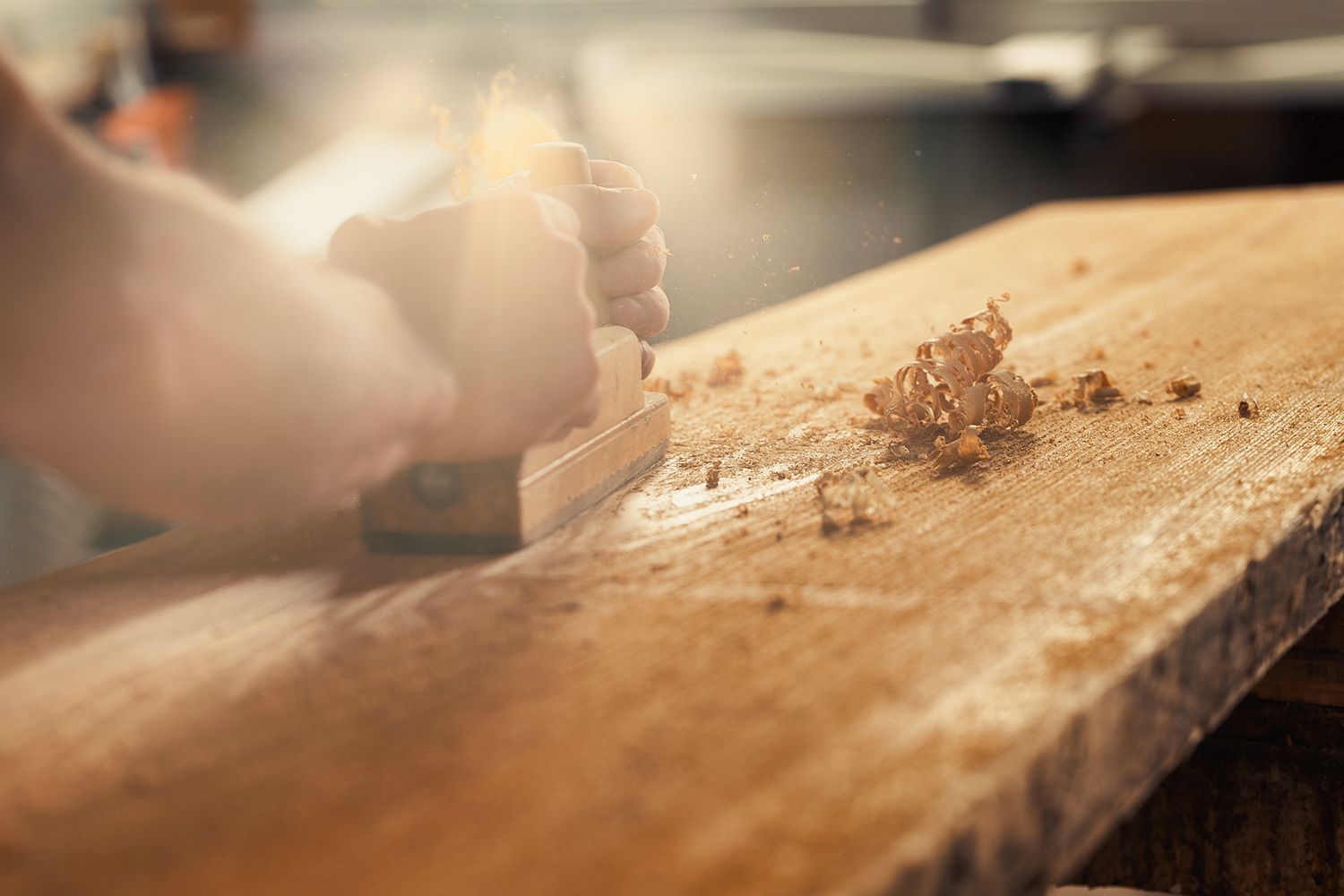 Close-up of a carpenter using a hand plane on a wooden plank, creating wood shavings. Close-up of a carpenter using a hand plane on a wooden plank, creating wood shavings.
