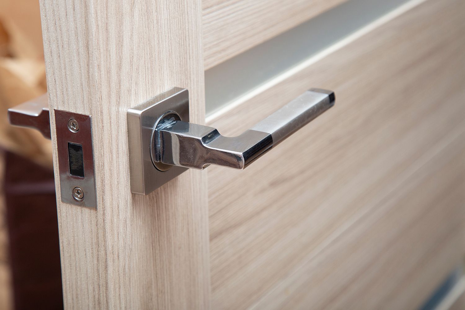 Silver door handle and latch on a light wood door, partially open. Silver door handle and latch on a light wood door, partially open.