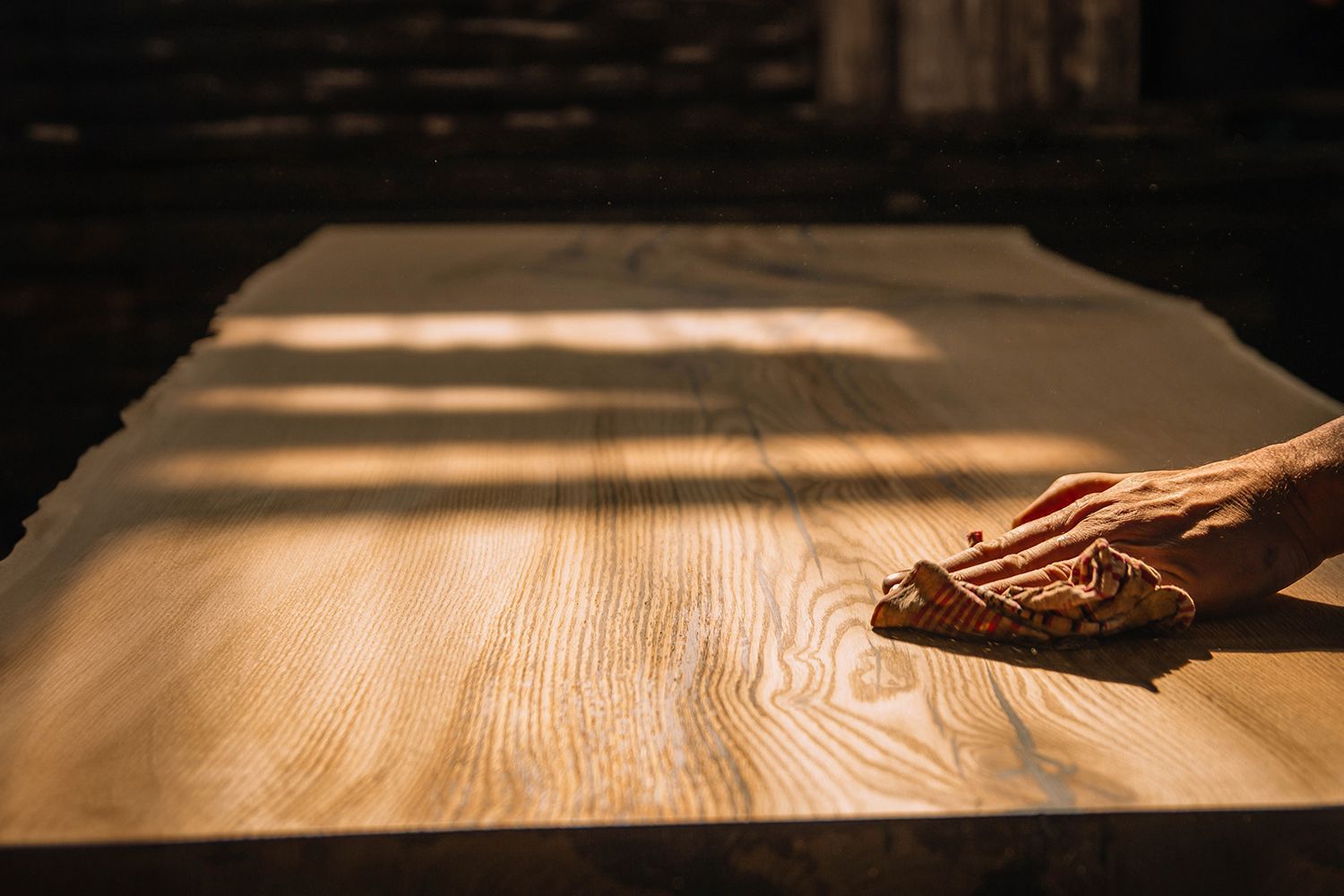 A hand sanding a large, unfinished wooden table, illuminated by sunlight. A hand sanding a large, unfinished wooden table, illuminated by sunlight.