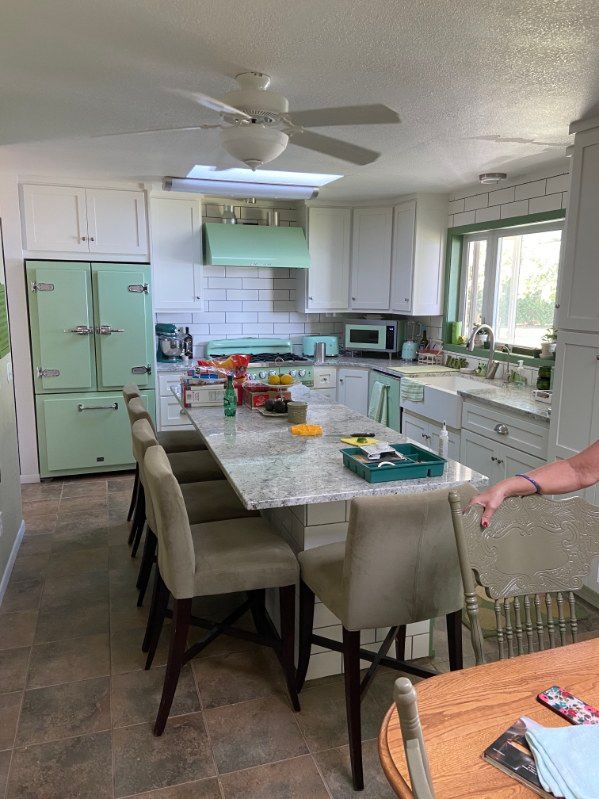 Spacious kitchen with a light green refrigerator, stove hood, and island. White cabinets, granite counters, and bar stools.