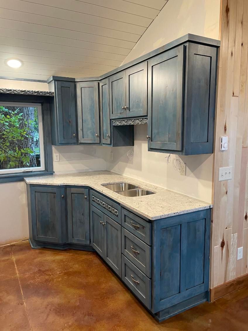 Blue kitchen cabinets with white countertops and a stainless steel sink in a corner.