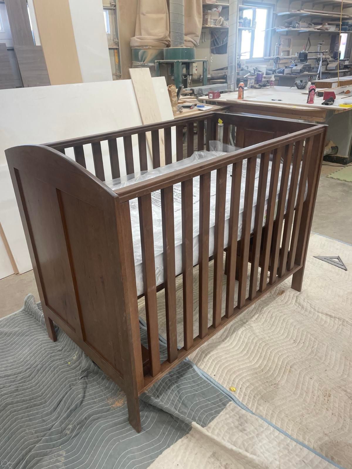 Wooden baby crib with a mattress, in a workshop setting.