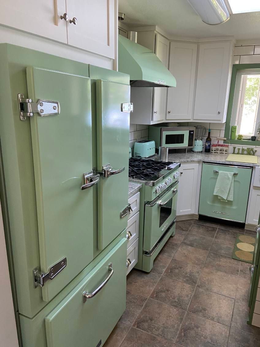 Green vintage kitchen with refrigerator, stove, and range hood. White cabinets and a brown tiled floor.