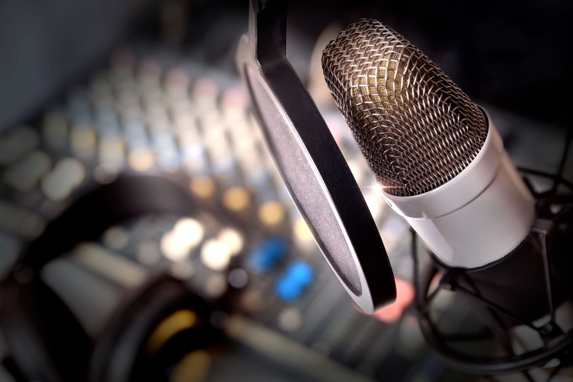 Microphone with pop filter, blurred audio mixing board in background.