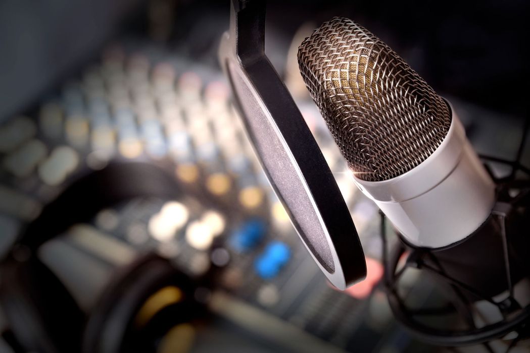 Microphone with pop filter, blurred audio mixing board in background.