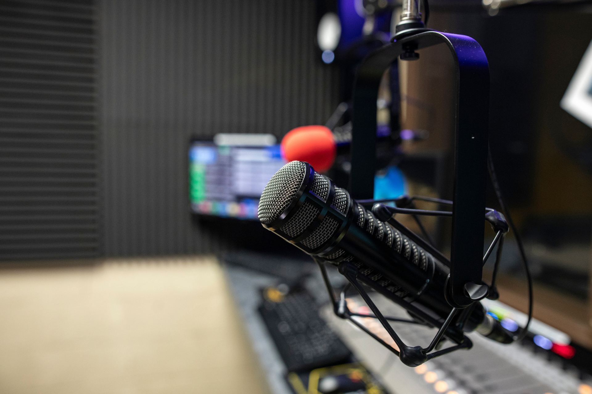 Microphone in a radio studio; audio equipment visible in the background.