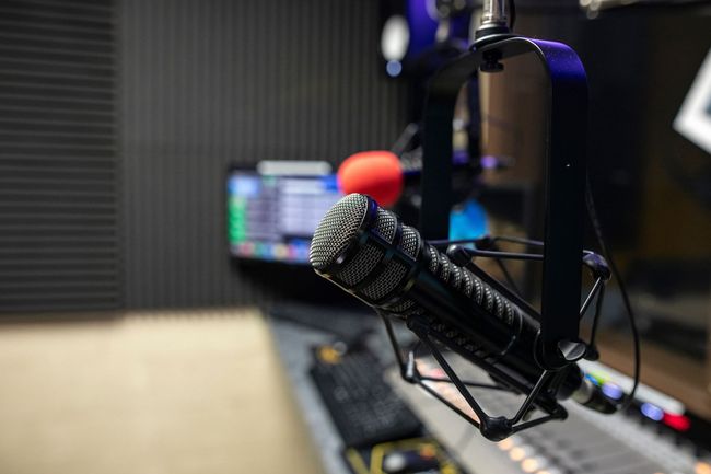 Microphone in a radio studio; audio equipment visible in the background.