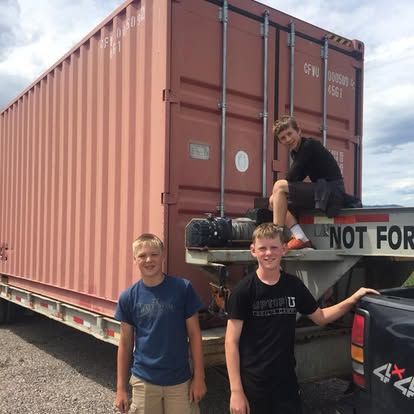 Two boys are standing in front of a large shipping container that says not for