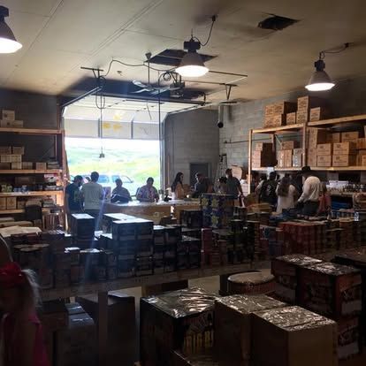 A group of people are standing in a warehouse filled with boxes of fireworks.