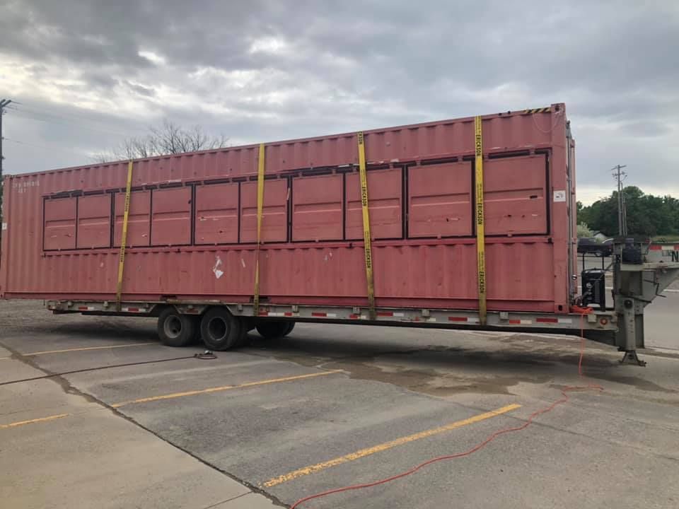 A red shipping container is on a trailer in a parking lot.