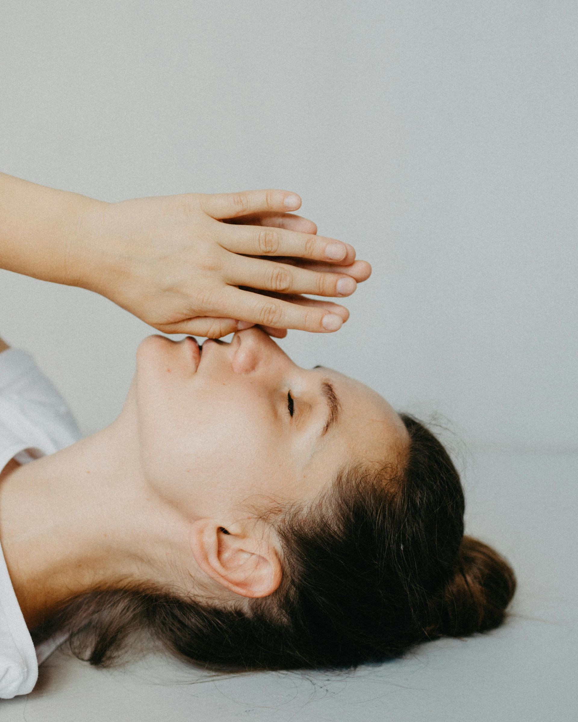 A women lying on the ground. We can see her head. She is bringing her palms together in prayer and lifting her hands up to her face with her eyes closed.