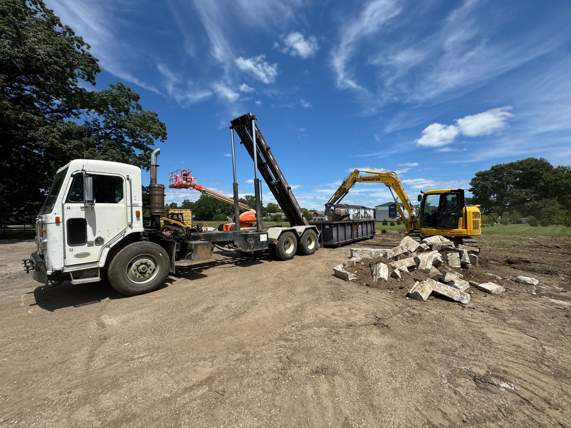 A dump truck is being towed by an excavator in a dirt field.