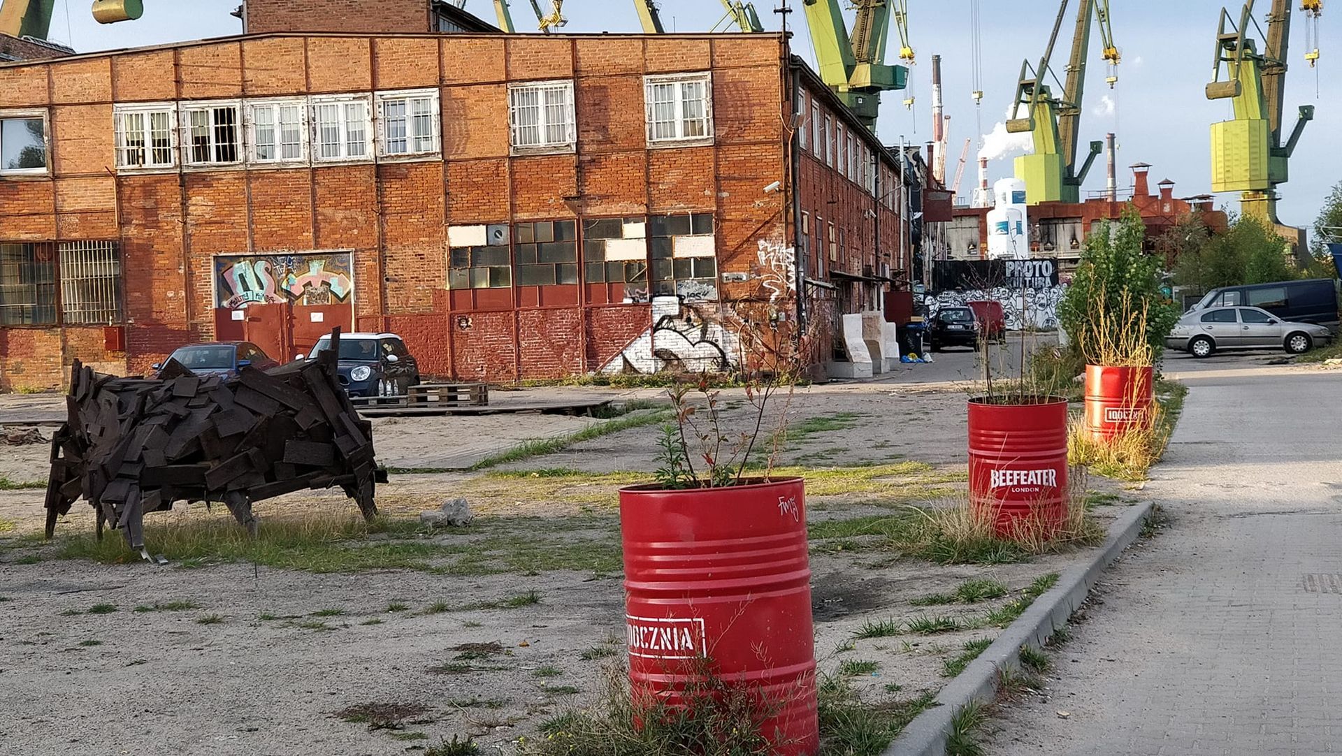 oljefat som planteringskärl och en skulptur av metallskrot vid ett hamnområde i Gdansk