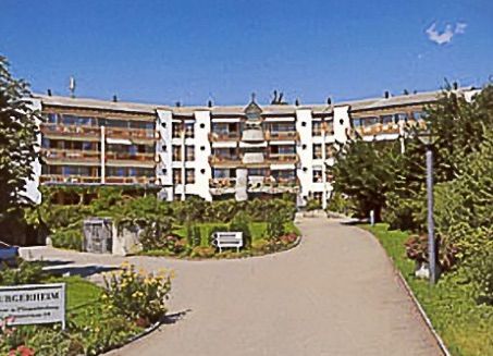 Ein großes Gebäude mit vielen Fenstern ist von Bäumen und Blumen umgeben.