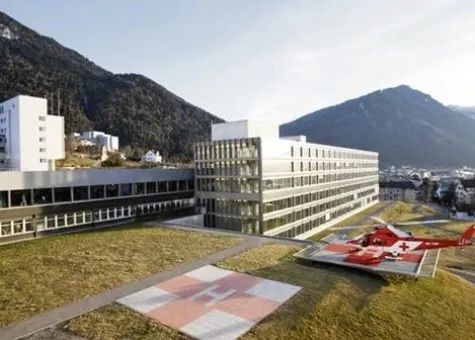 Ein roter Hubschrauber steht auf einem Hubschrauberlandeplatz vor einem großen Gebäude.