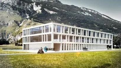 Ein großes Gebäude steht mitten auf einer Wiese vor einem Berg.