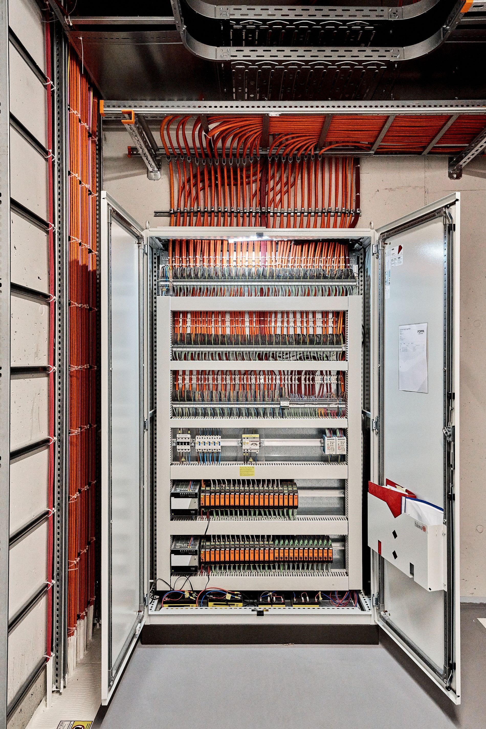 Ein großer Schaltschrank mit offenen Türen und vielen Kabeln, die von der Decke hängen.