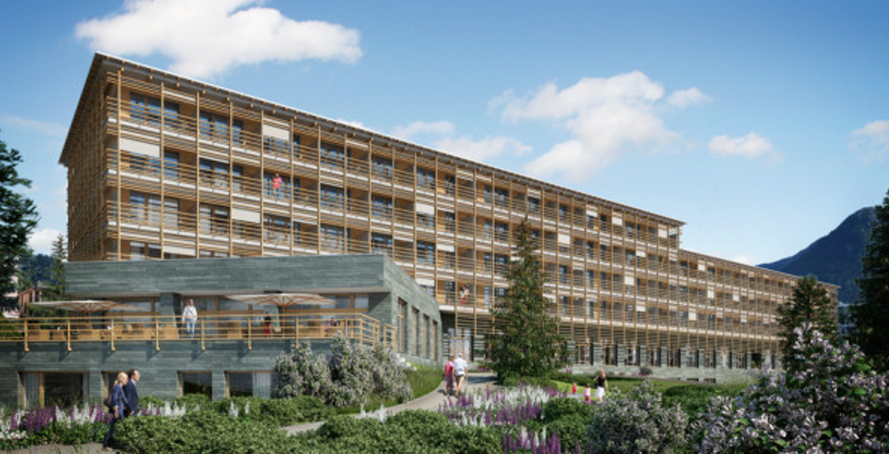 Ein großes Gebäude mit vielen Fenstern ist von Bäumen und Blumen umgeben.