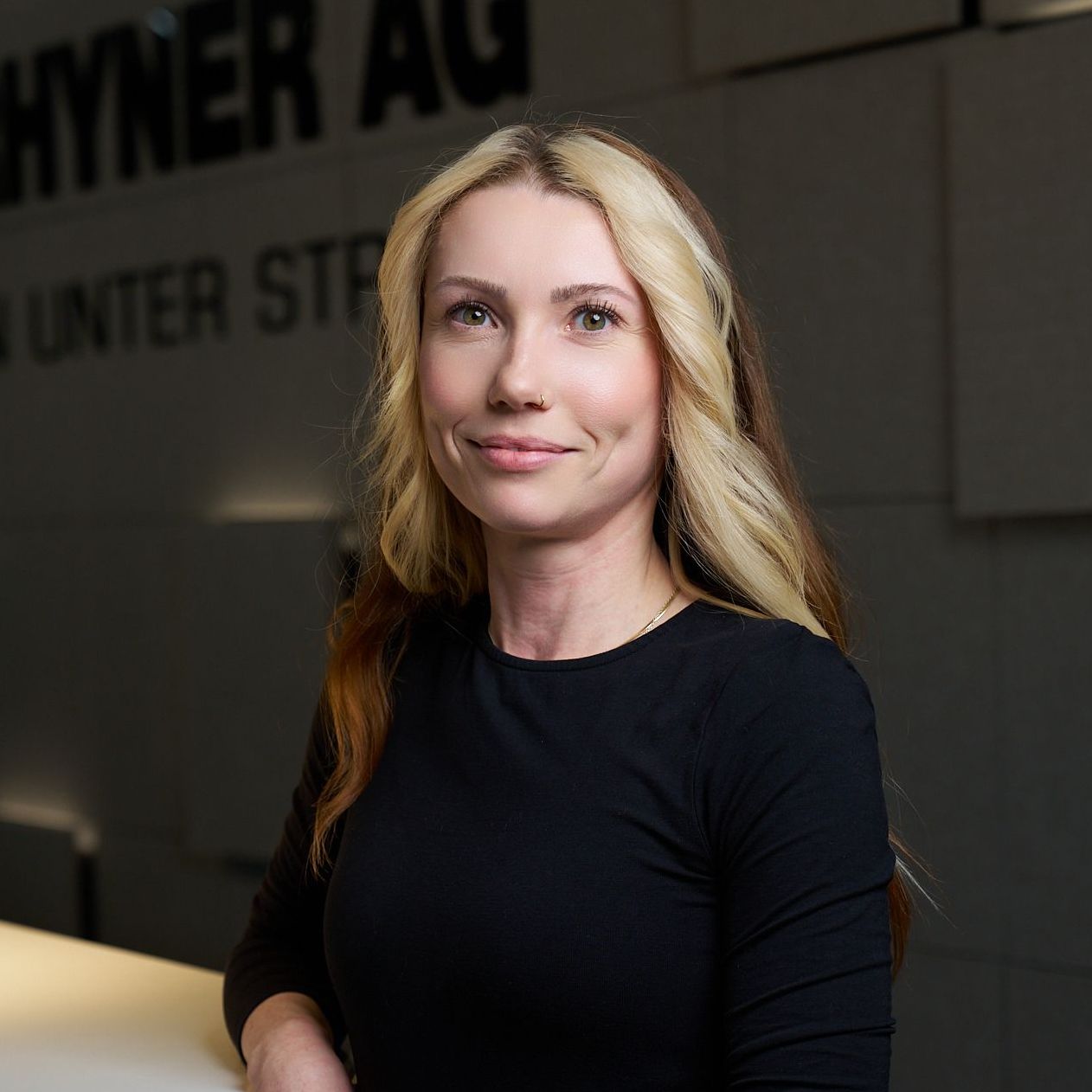Eine Frau in einem schwarzen Hemd steht vor einem Schild mit der Aufschrift „Hyner AG“.