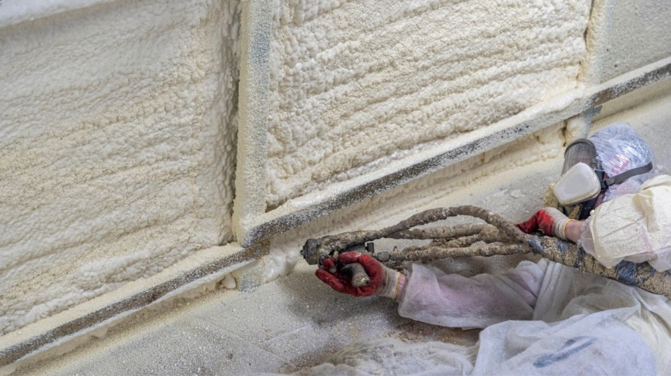 Worker applying spray foam material along interior wall seams inside a post frame building.