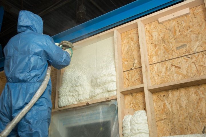 Person in protective suit sprays foam insulation onto a wall.