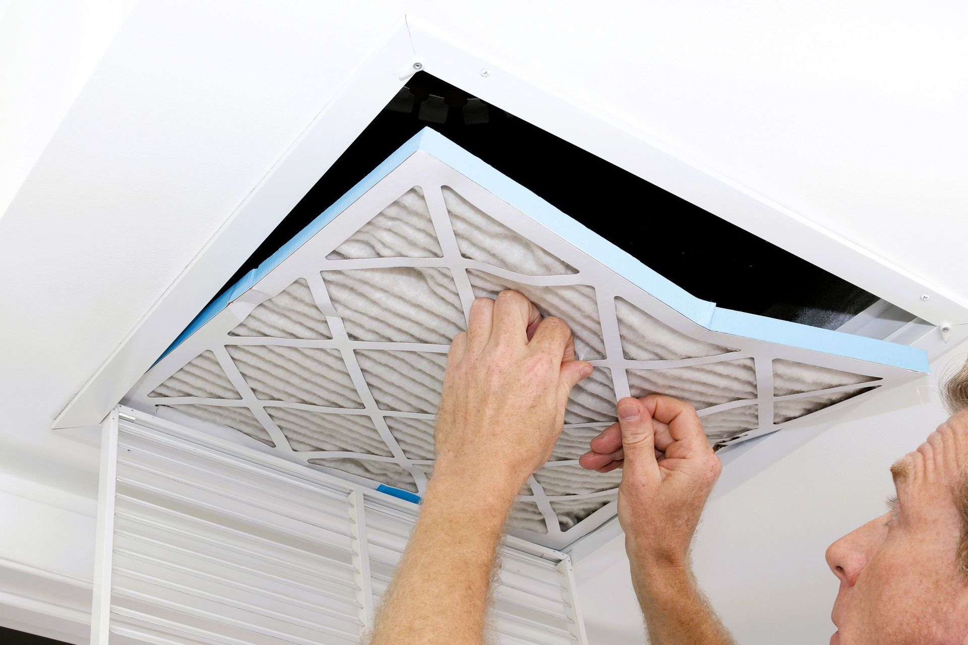 Person installing air filter in ceiling unit for air filter maintenance