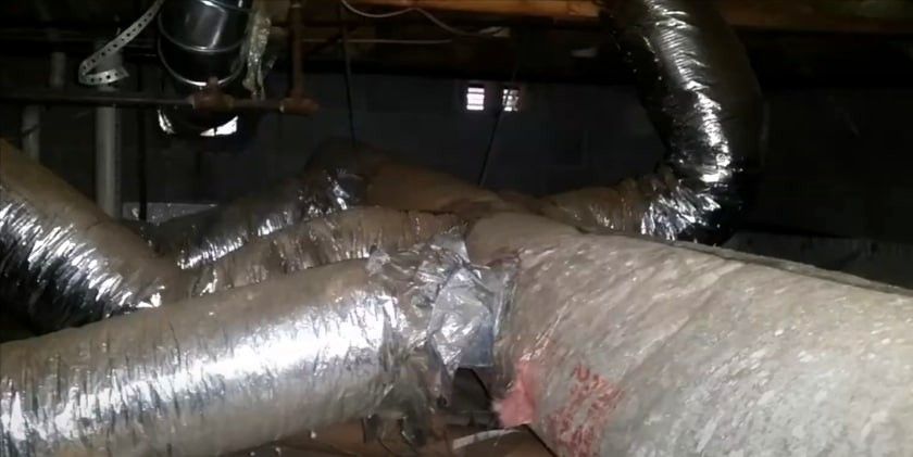 Damaged HVAC ductwork in a basement caused by pest infestation, showing torn insulation.