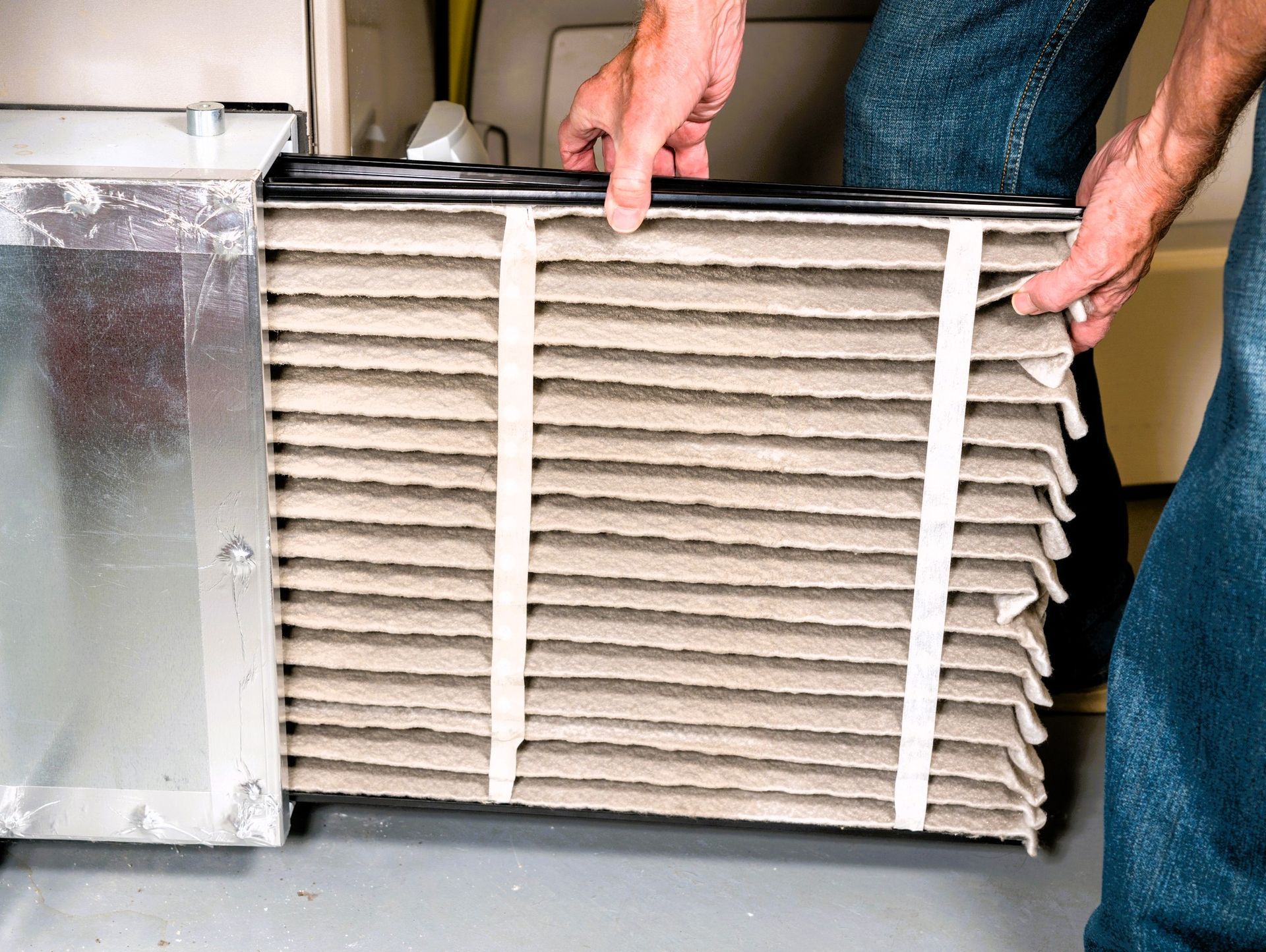 Technician holding dirty air filter next to furnace for maintenance