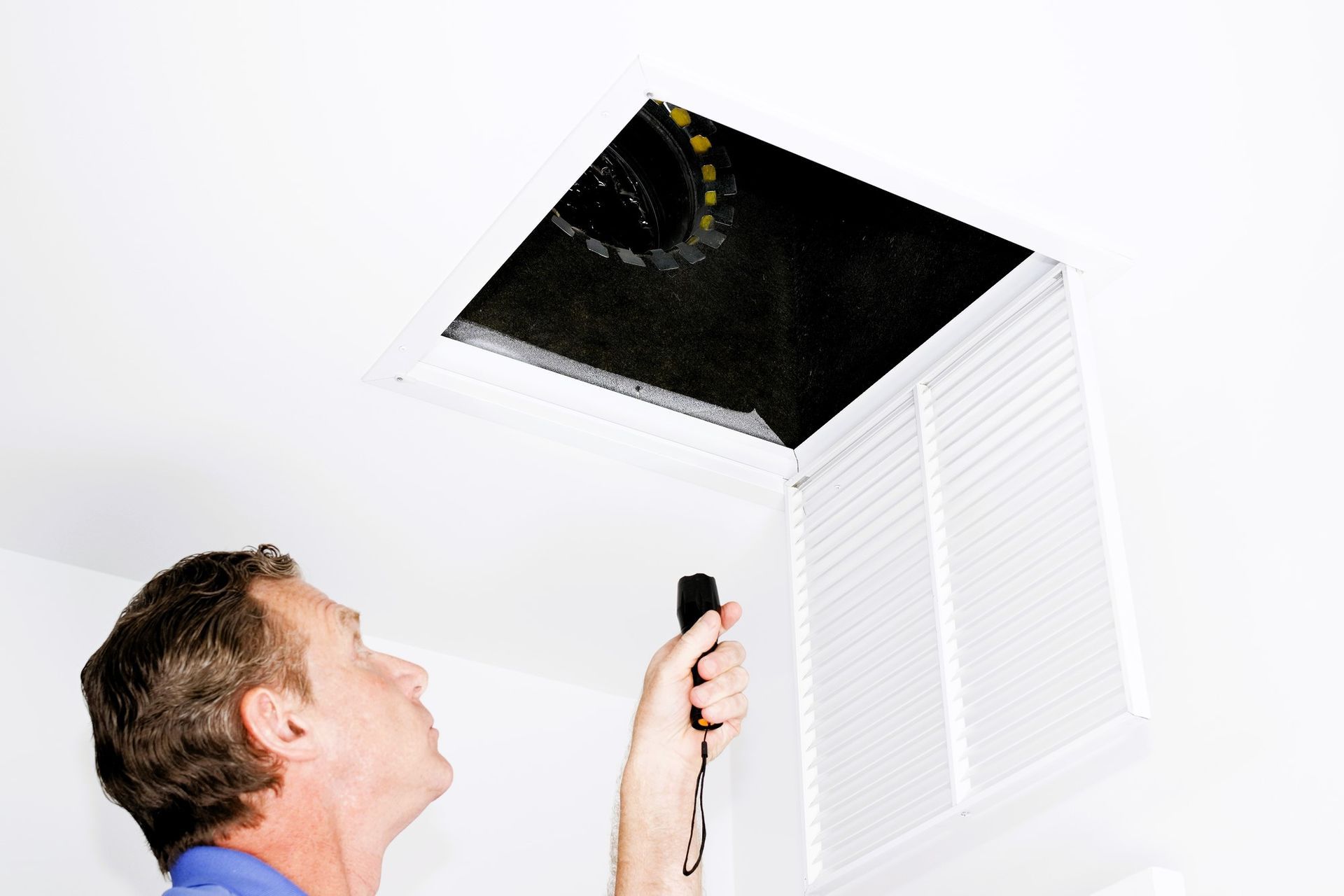 Person holding a remote control near an open ceiling air vent