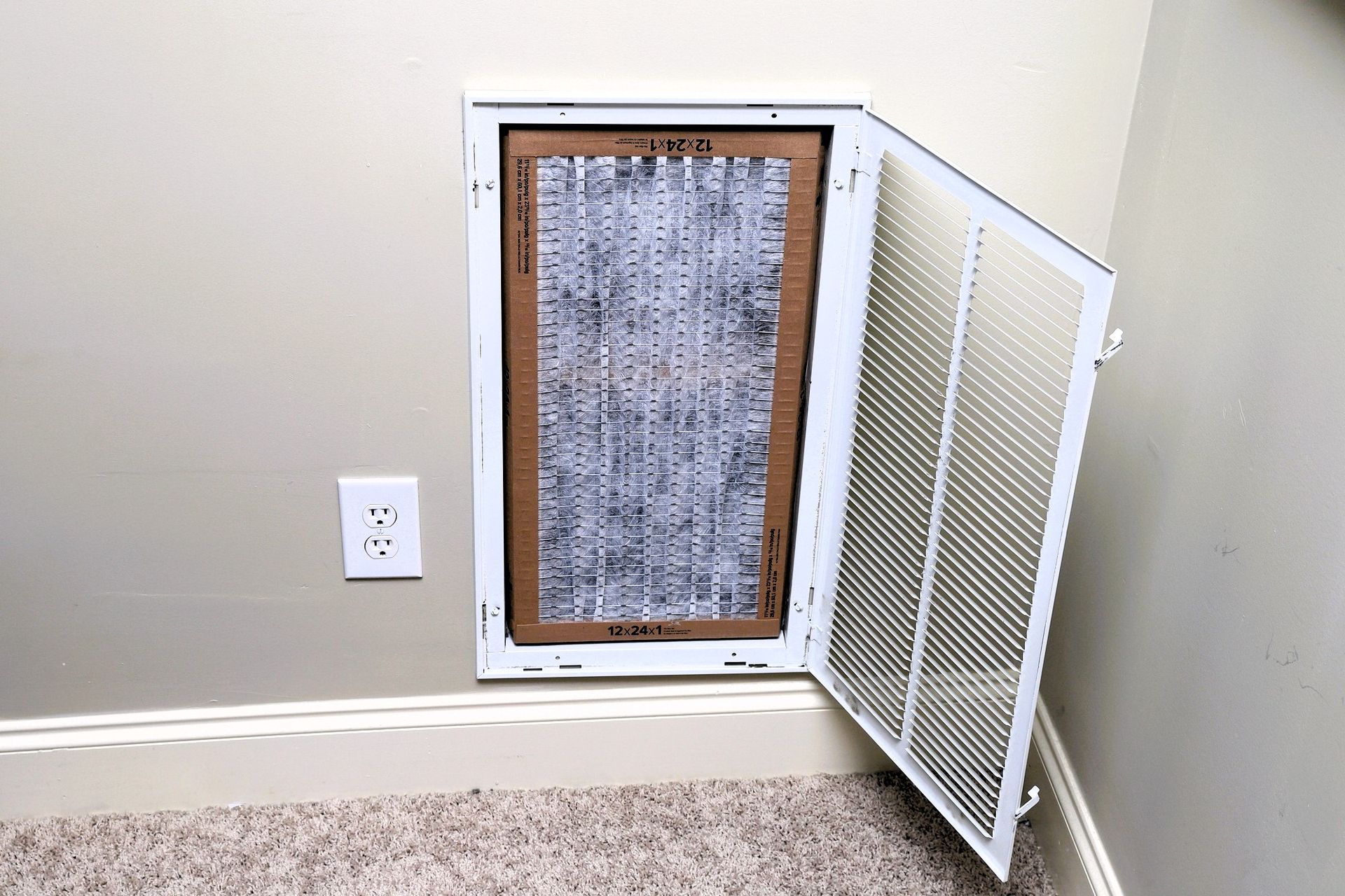 Open HVAC return air vent with dirty filter exposed on a carpeted floor