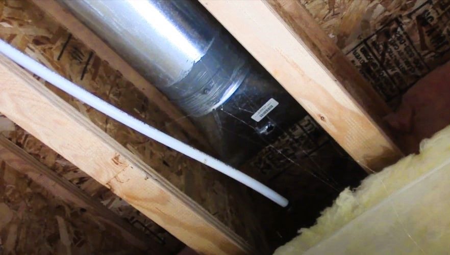 Interior view of attic space showing insulation, wooden beams, and common ductwork repairs