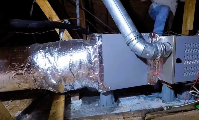 Close-up of HVAC ductwork with silver insulation and furnace unit in attic