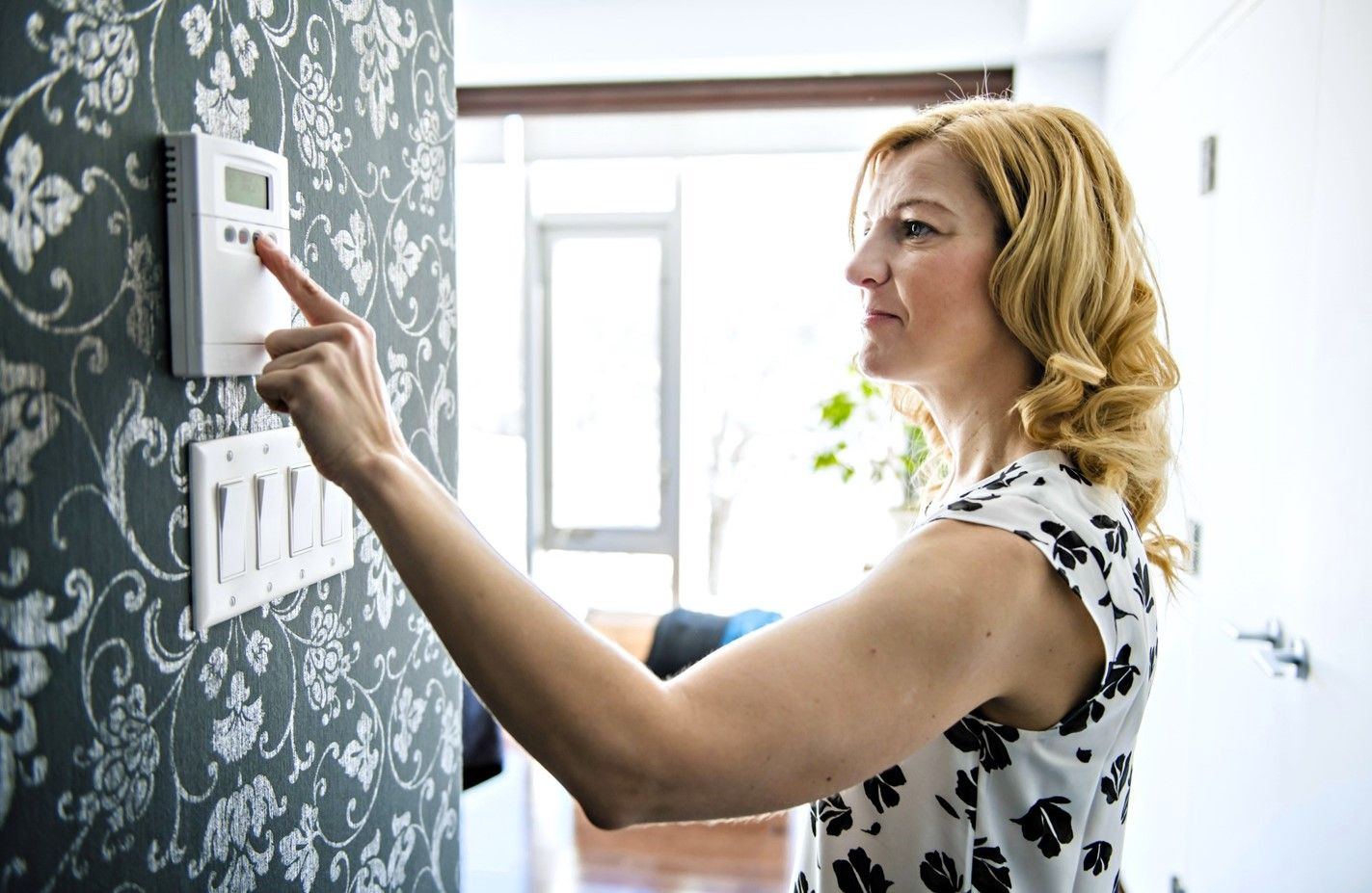 A woman adjusting a programmable thermostat for home heating 