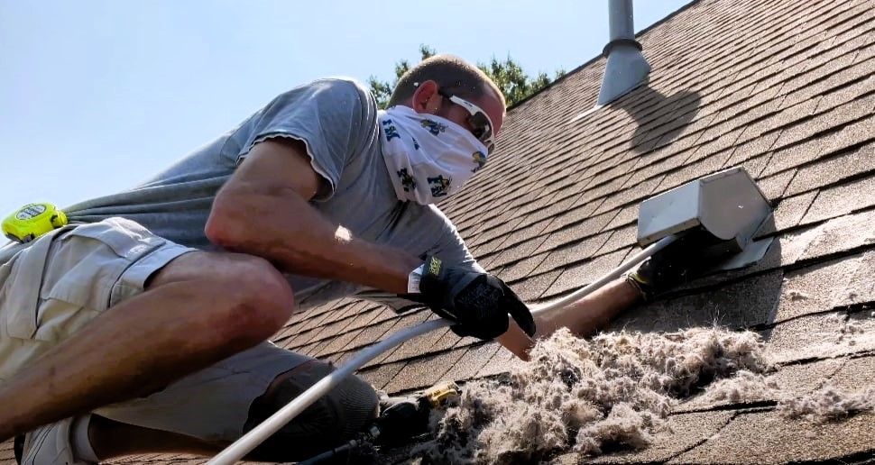 Man cleaning a roof dryer vent on top of a house in Grand Rapids