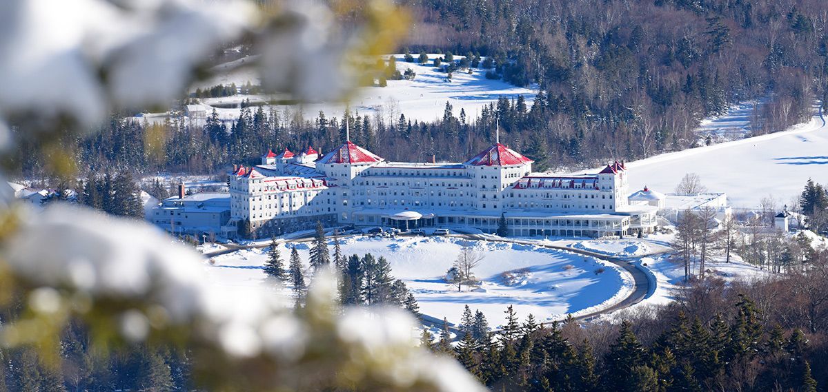 A large building is surrounded by snow covered trees in the middle of a snowy forest.