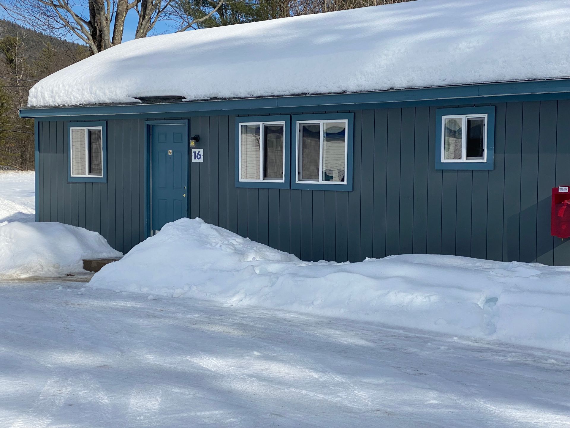 A blue house with snow on the roof and a red mailbox in front of it.