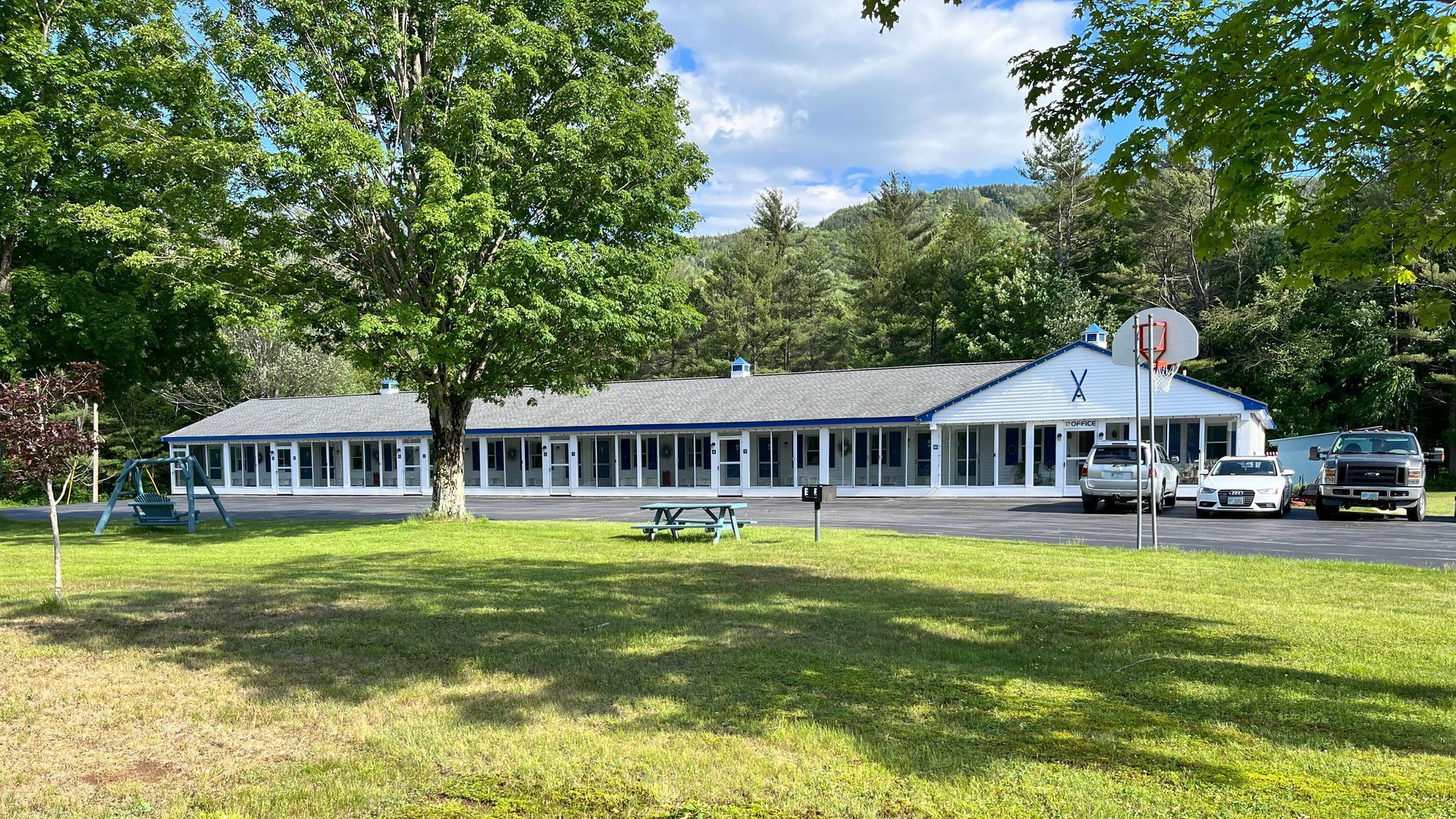 A large house with a picnic table in front of it is surrounded by trees.