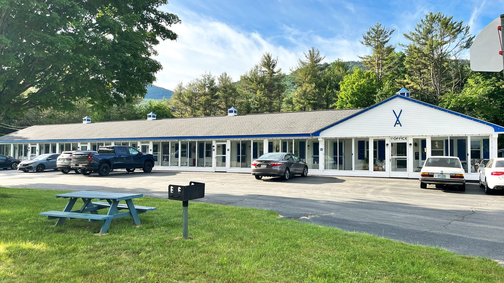 A motel with cars parked in front of it and a picnic table in front of it.