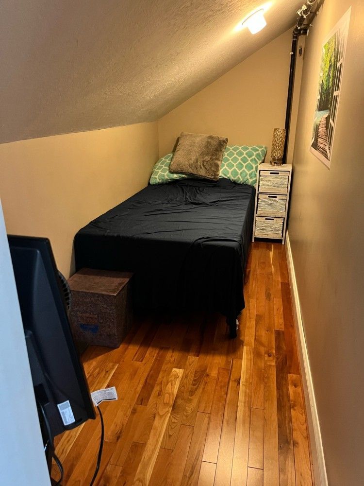 A small bedroom with a bed , nightstand , and television.