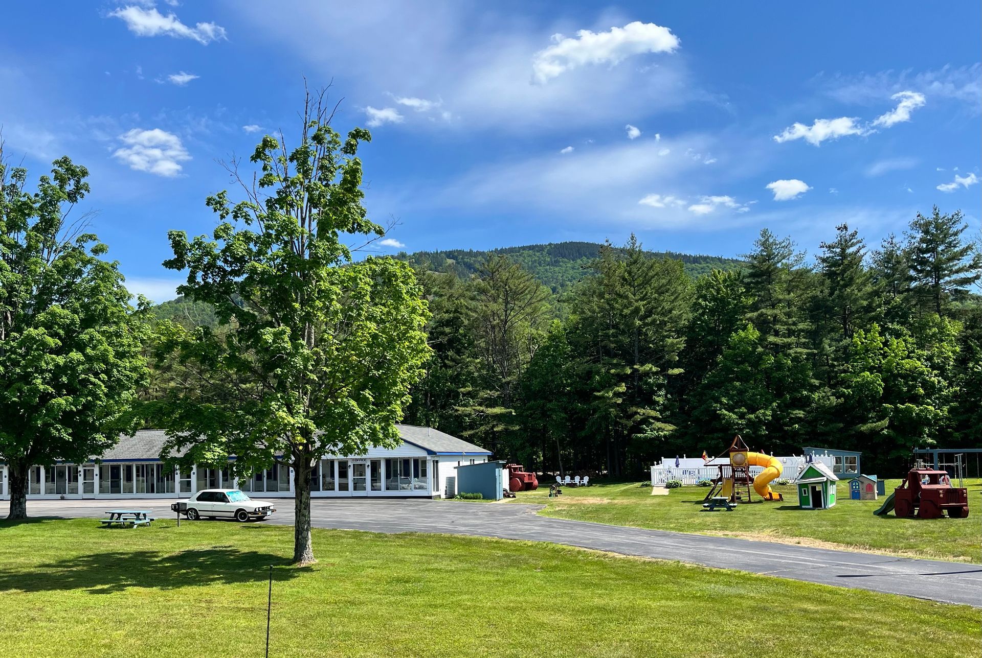 A large grassy field with a motel in the background and a mountain in the background.